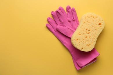 Sponge and gloves on yellow background, top view. Space for text