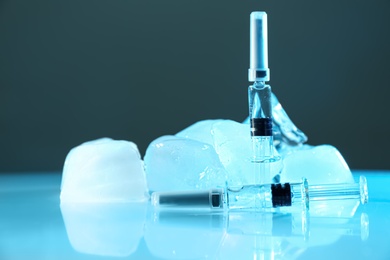 Photo of Syringes with COVID-19 vaccine and ice cubes on table