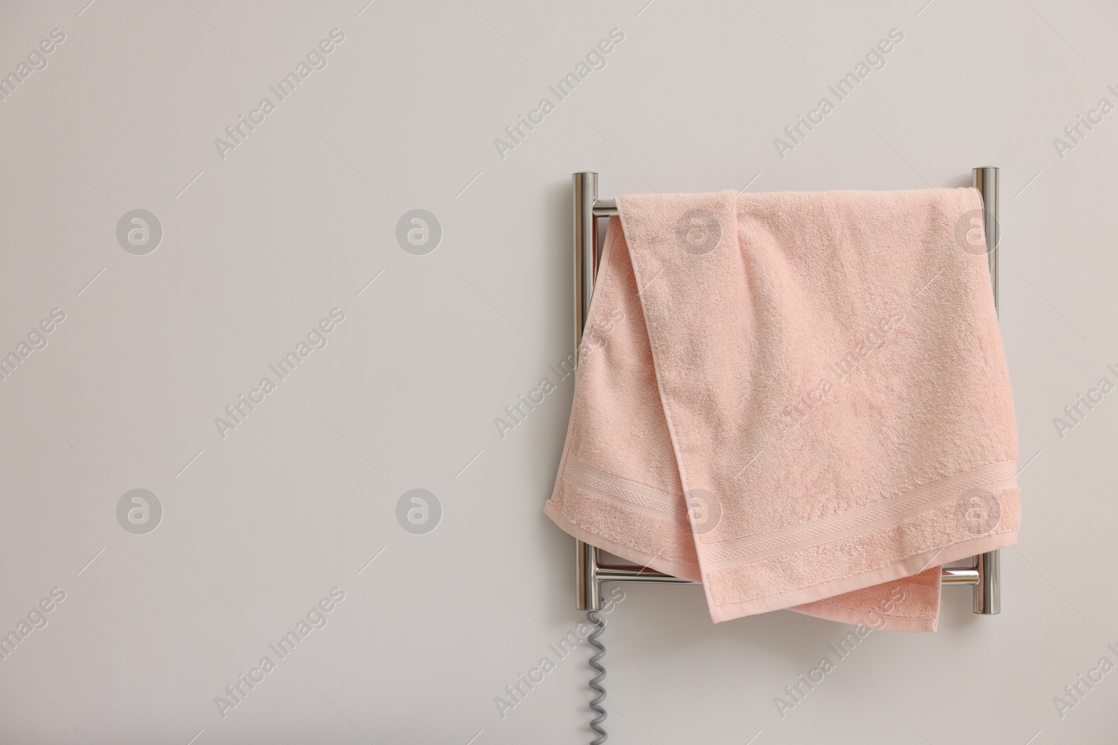 Photo of Heated rail with pink towel on white wall, space for text