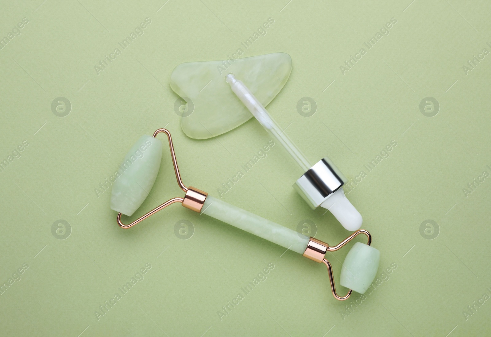 Photo of Jade gua sha tool, facial roller and dropper on light green background, flat lay