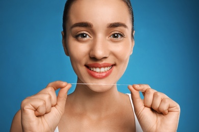 Photo of Young woman flossing her teeth on blue background. Cosmetic dentistry