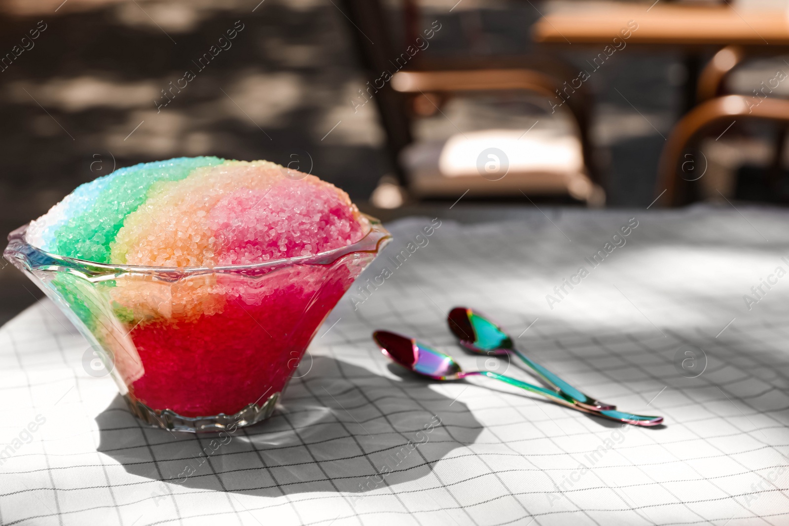 Photo of Rainbow shaving ice in glass dessert bowl and spoons on table outdoors