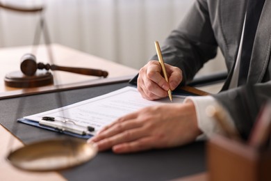 Notary writing notes at wooden table in office, closeup