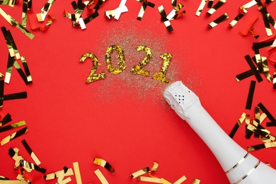 Photo of Flat lay composition with number 2021 made of shiny glitters near champagne bottle and confetti on red background