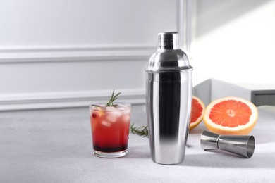 Photo of Metal shaker, delicious cocktail, jigger and grapefruit on light grey table, space for text