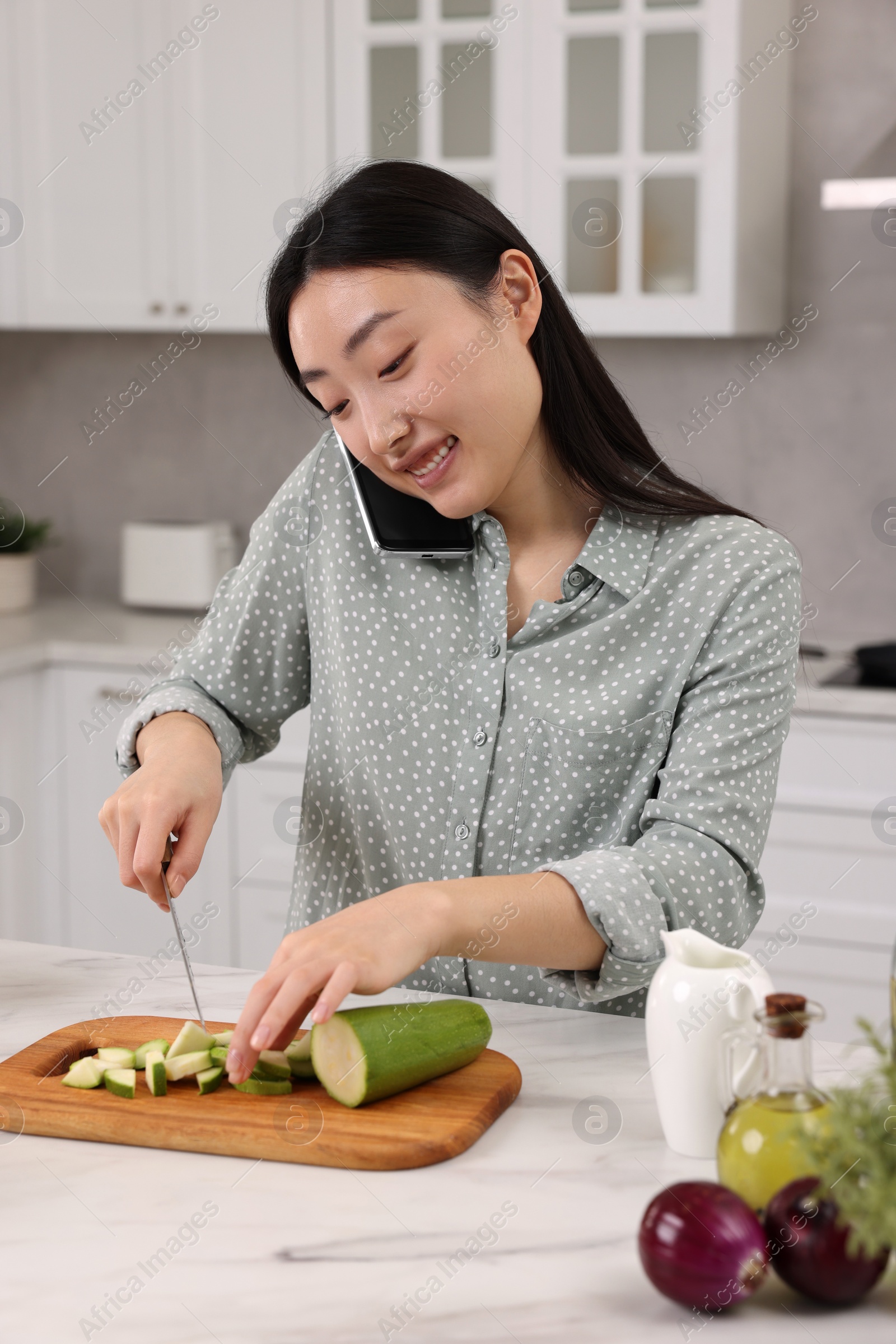 Photo of Smiling woman talking by smartphone while cooking in kitchen