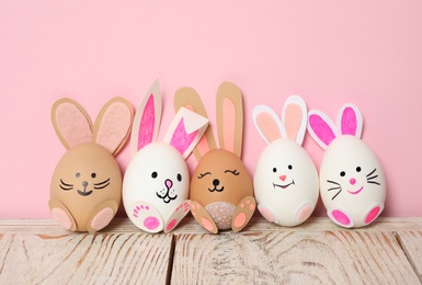 Photo of Eggs as cute bunnies on white wooden table against pink background. Easter celebration
