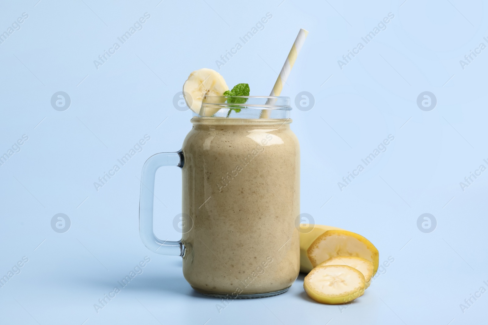 Photo of Mason jar with delicious fruit smoothie and fresh banana on light blue background