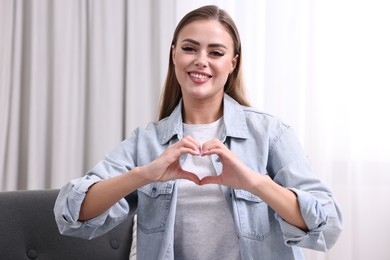 Happy woman showing heart gesture with hands indoors