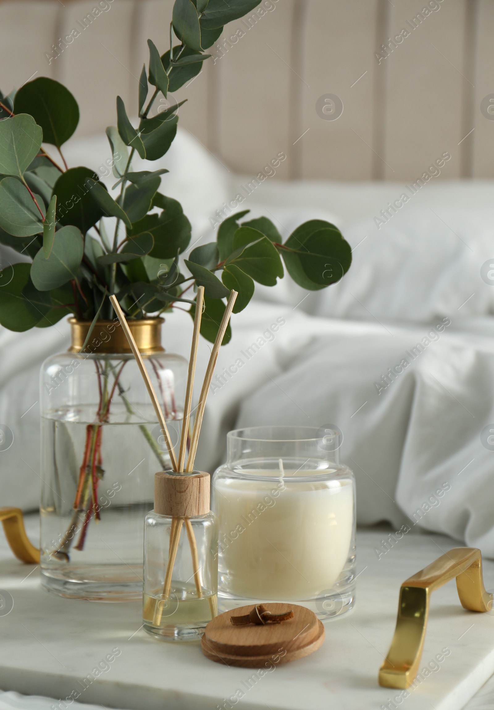 Photo of Eucalyptus branches, candle and aromatic reed air freshener on bed indoors, closeup. Interior elements