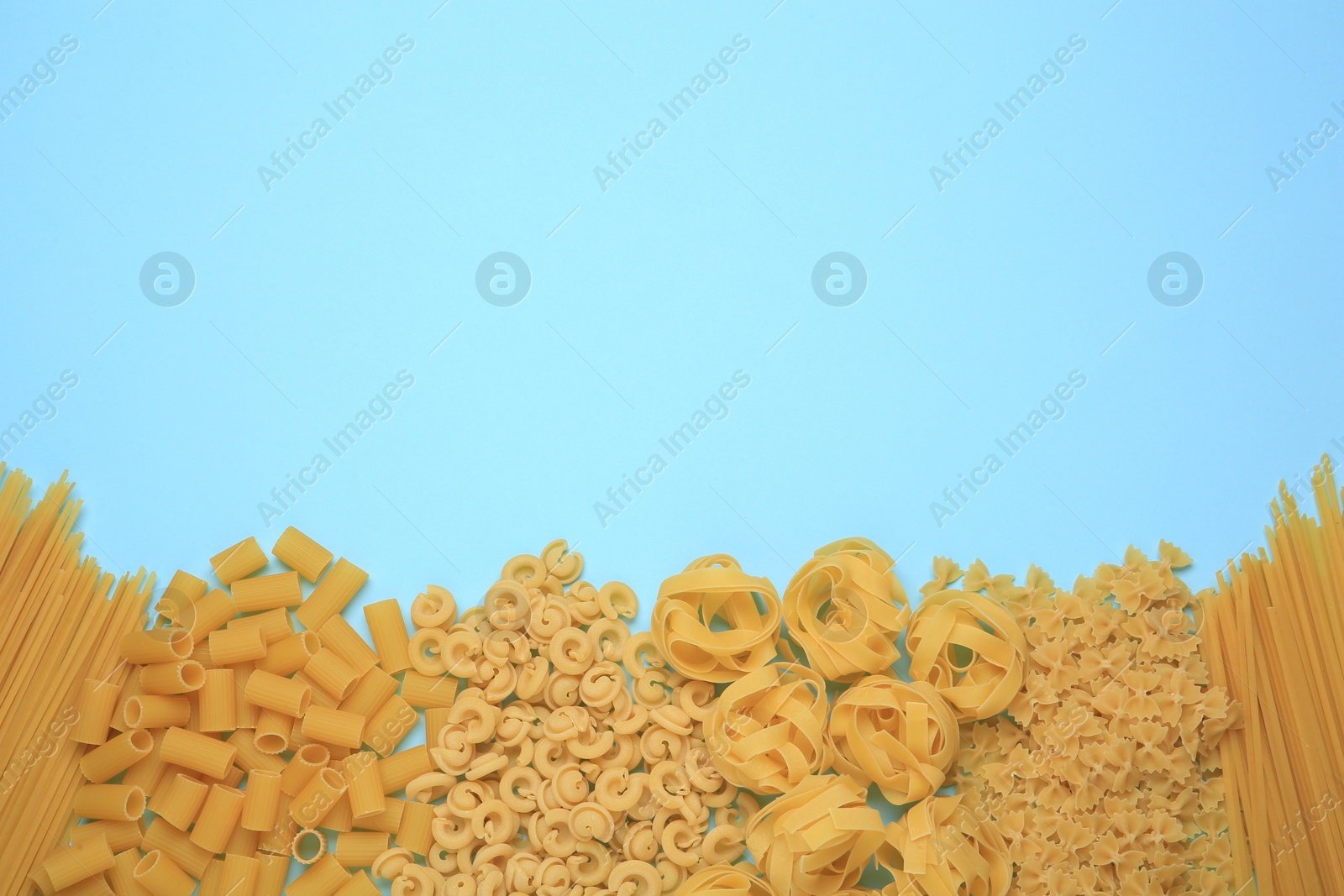 Photo of Different types of pasta on light blue background, flat lay. Space for text