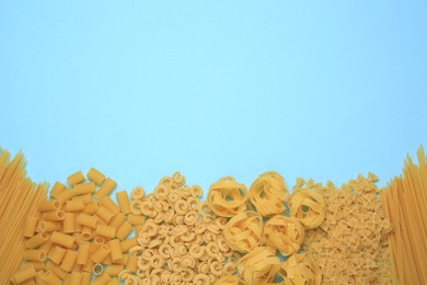 Different types of pasta on light blue background, flat lay. Space for text