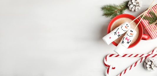 Flat lay composition with funny snowmen made of marshmallows in cup on white wooden table. Space for text