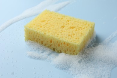 Yellow sponge with foam on light blue background, closeup