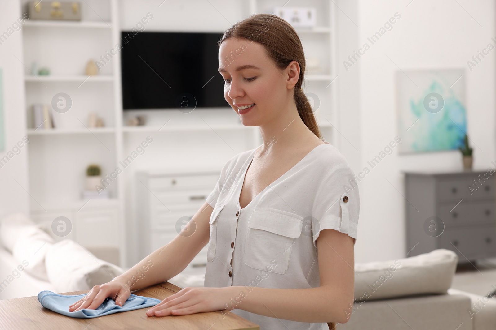 Photo of Woman with microfiber cloth cleaning wooden chest of drawers in room