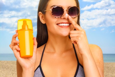 Image of Sun protection. Beautiful young woman applying sunblock onto face on beach, closeup