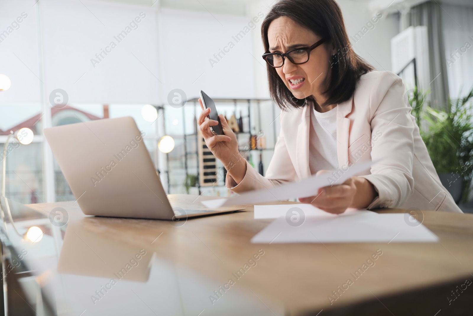Photo of Emotional businesswoman with smartphone near laptop in office. Online hate concept