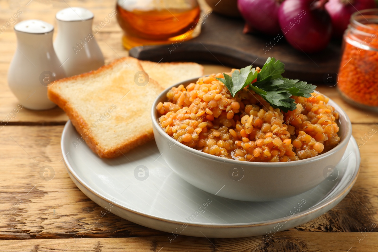 Photo of Delicious red lentils with parsley in bowl served on wooden table, closeup