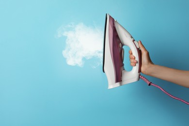 Woman holding modern iron with steam on turquoise background, closeup. Space for text