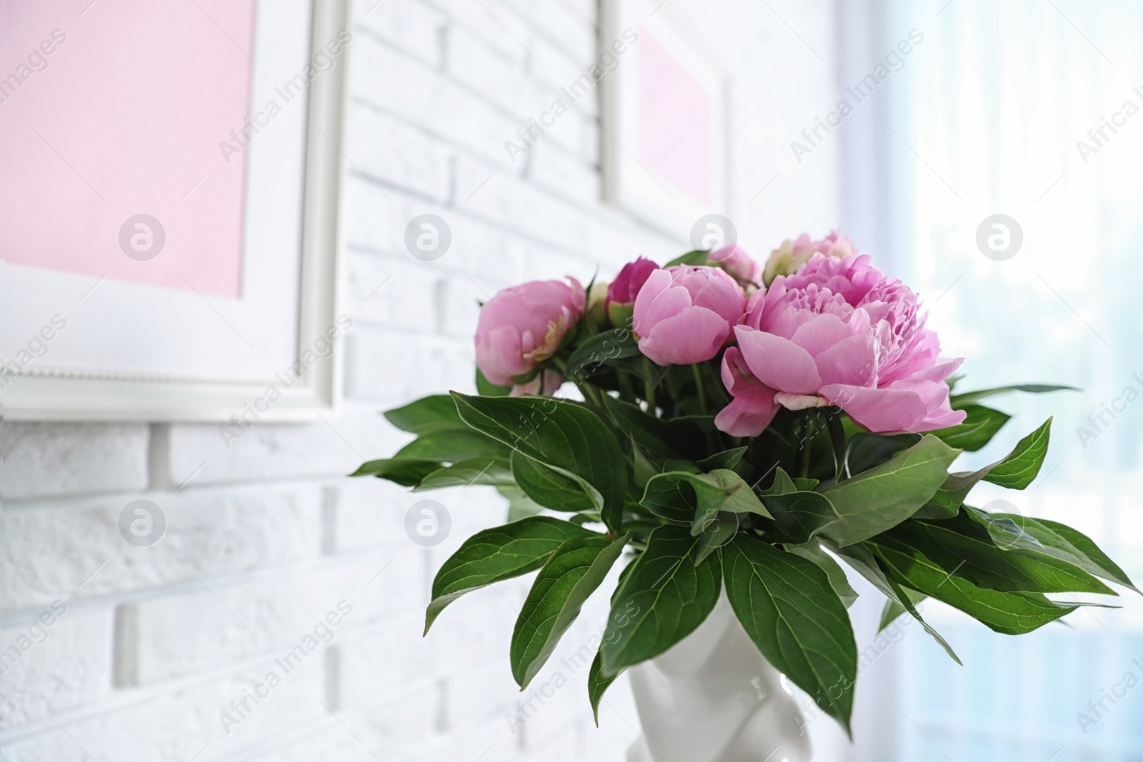 Photo of Vase with bouquet of beautiful peonies at white wall in room, space for text