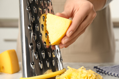 Woman grating fresh cheese at table, closeup