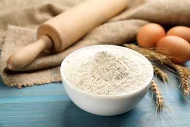 Photo of Wheat flour in bowl on light blue wooden table