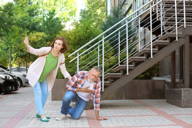 Woman helping mature man suffering from heart attack, outdoors