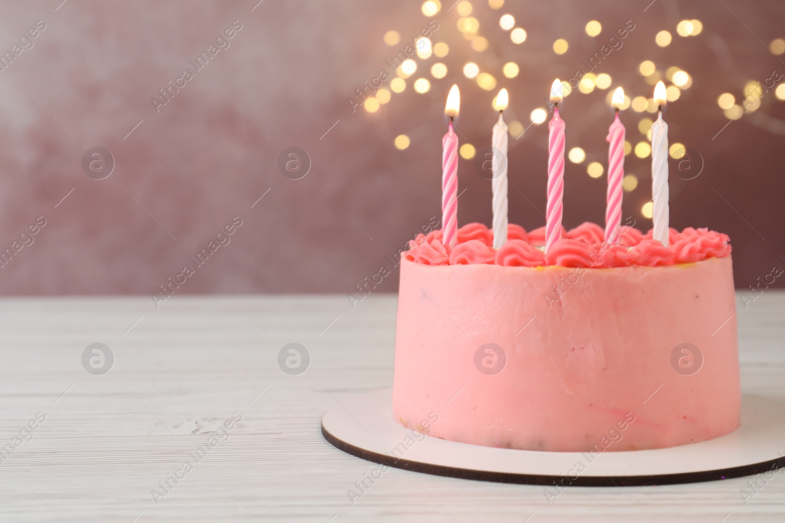 Photo of Cute bento cake with tasty cream and burning candles on white wooden table. Space for text