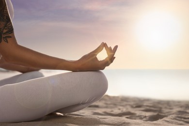 Image of Young woman meditating on beach at sunrise, closeup. Practicing yoga