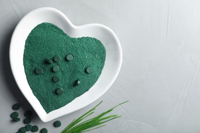 Photo of Plate of spirulina powder, pills and grass on grey background, top view with space for text