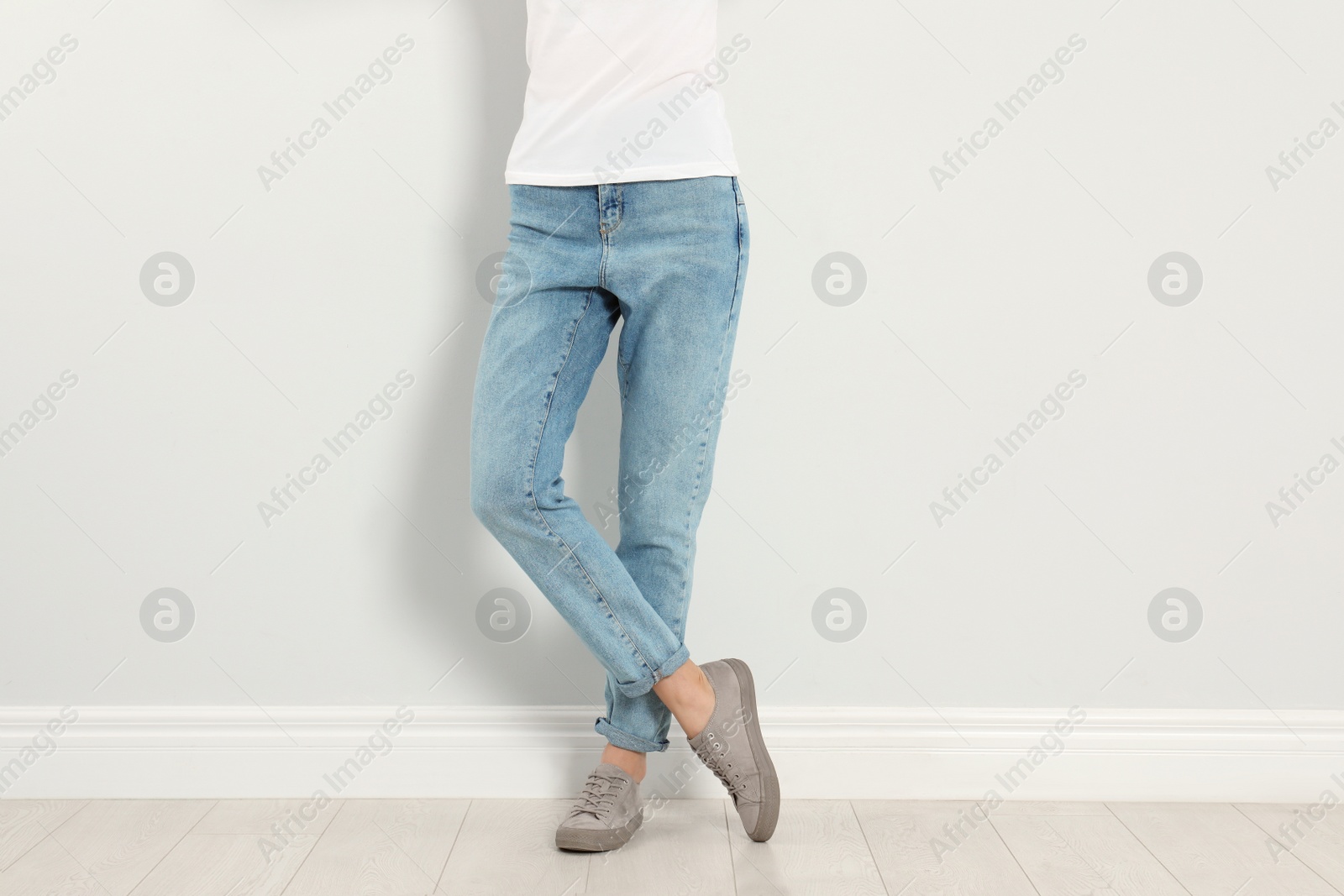 Photo of Young woman in stylish jeans near light wall, closeup