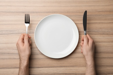 Photo of Man with empty plate and cutlery at wooden table, top view