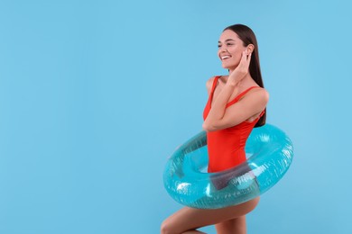 Photo of Young woman in stylish swimsuit with inflatable ring on light blue background, space for text