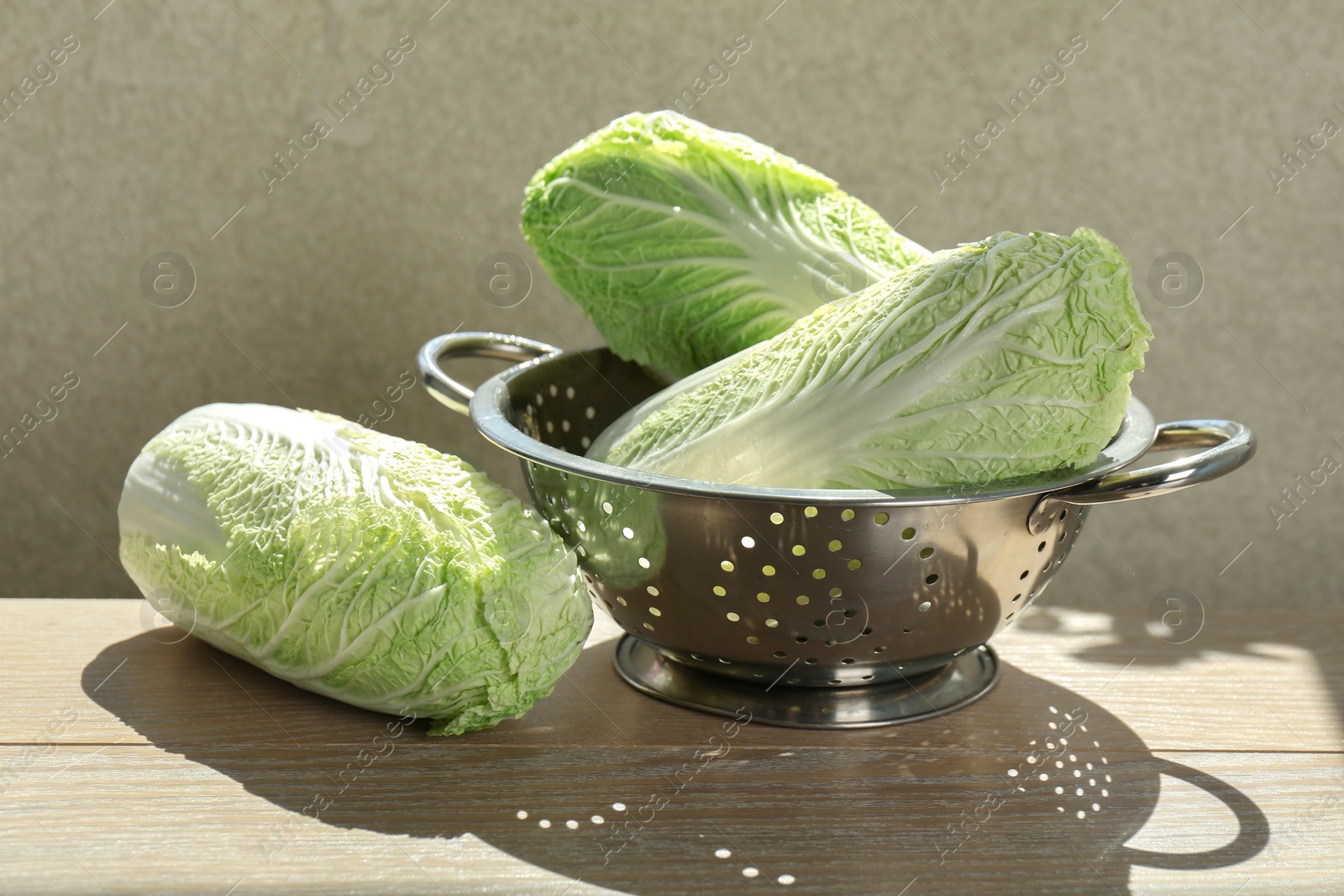 Photo of Fresh Chinese cabbages and colander on light wooden table indoors