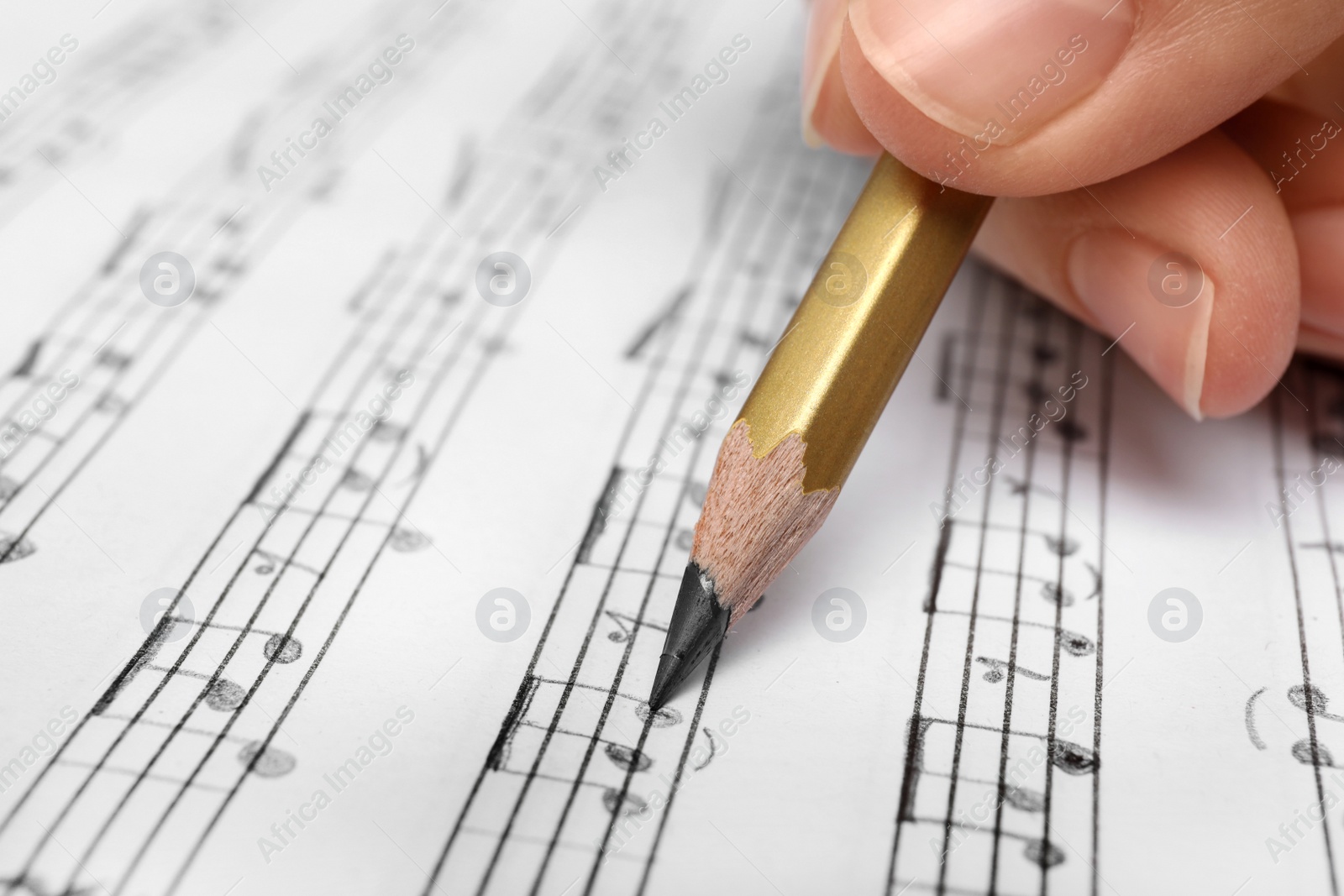 Photo of Woman writing music notes on sheet with pencil, closeup