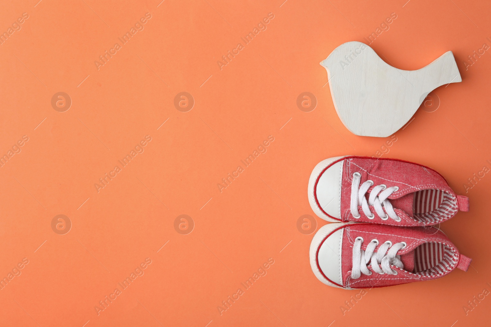 Photo of Child's shoes and wooden toy on coral background, flat lay with space for text