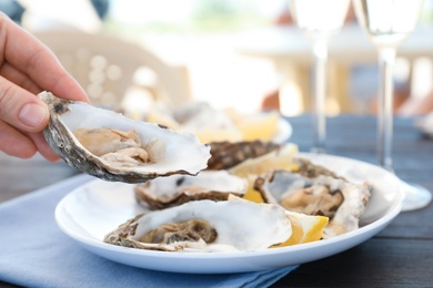 Photo of Woman with fresh oyster over plate, focus on hand