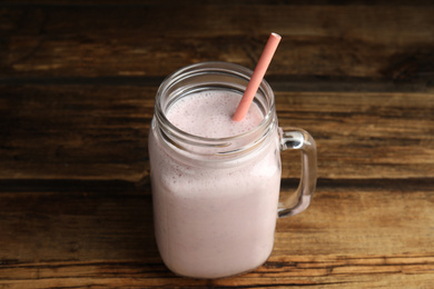 Photo of Tasty milk shake with straw in mason jar on wooden table