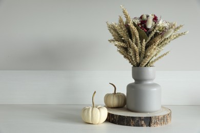 Beautiful bouquet of dry flowers and small pumpkins on white table near light wall, space for text