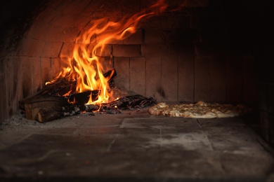 Photo of Burning firewood and tasty pizza in oven at restaurant kitchen