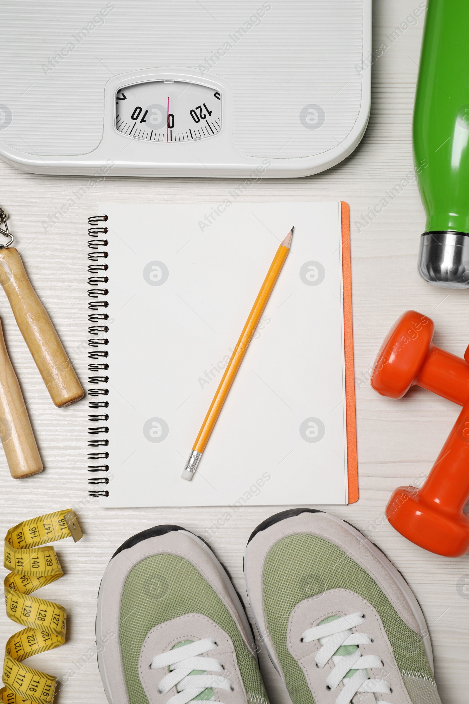 Photo of Notebook, scales and sports equipment on white wooden table, flat lay. Personal training