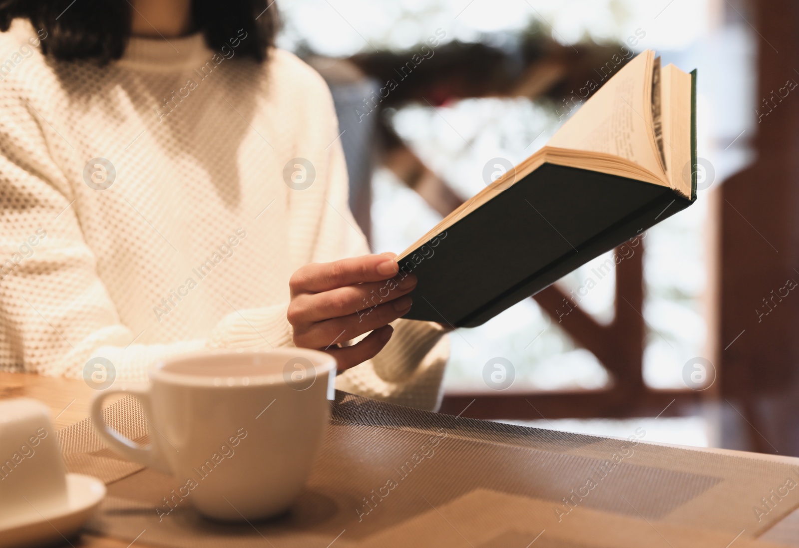 Photo of Woman with coffee reading book at wooden table, closeup