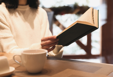 Woman with coffee reading book at wooden table, closeup