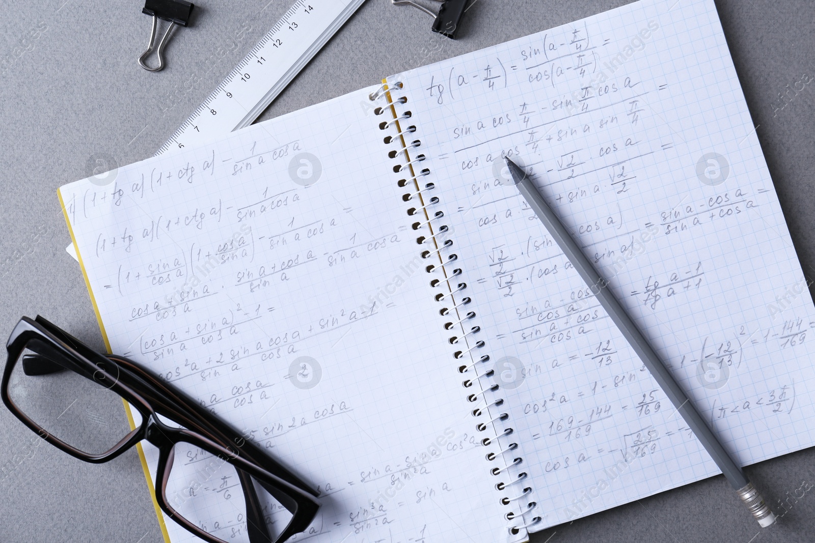 Photo of Notebook, pencil and glasses on light grey table, flat lay. Doing homework