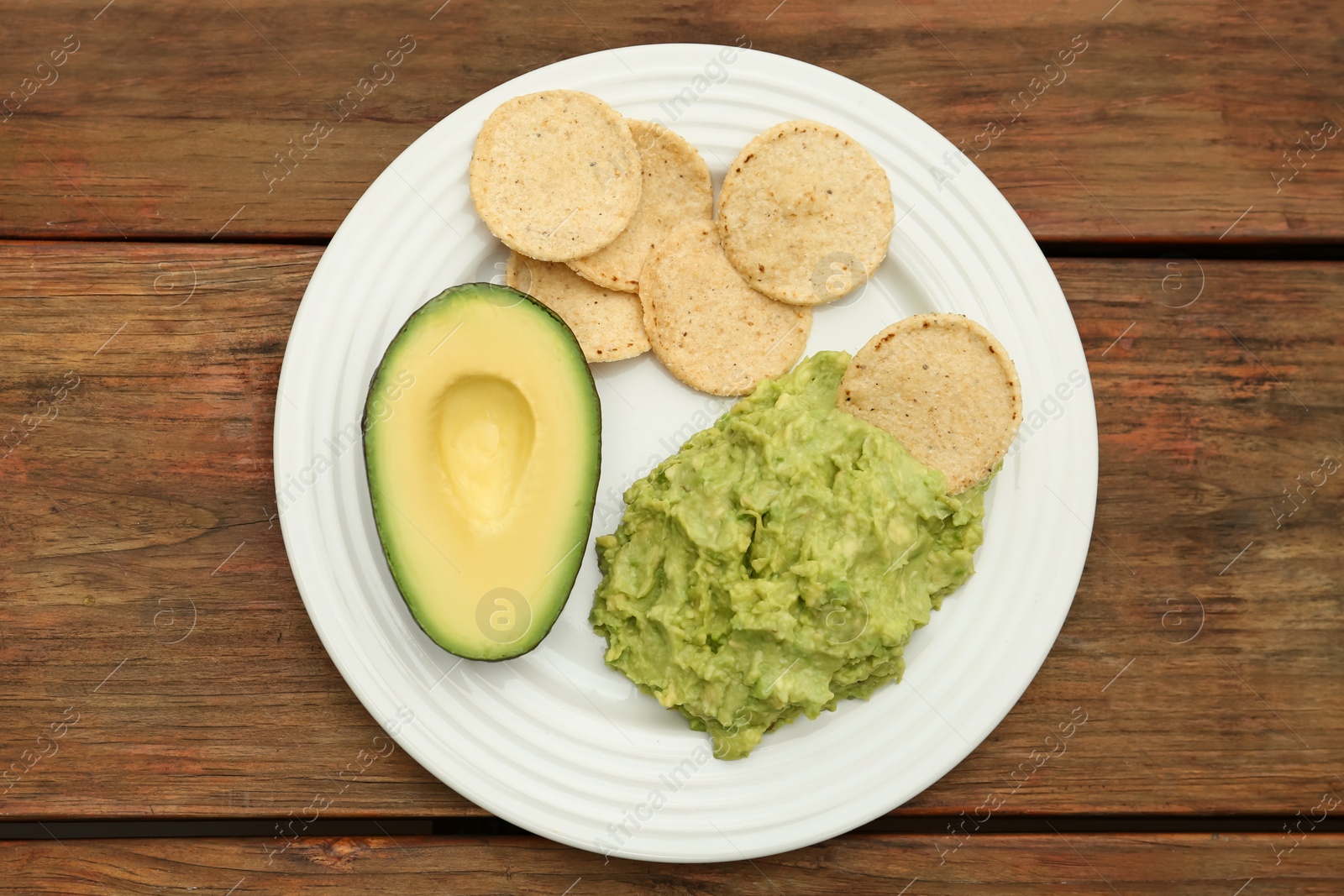 Photo of Delicious guacamole, avocado and chips on wooden table, top view