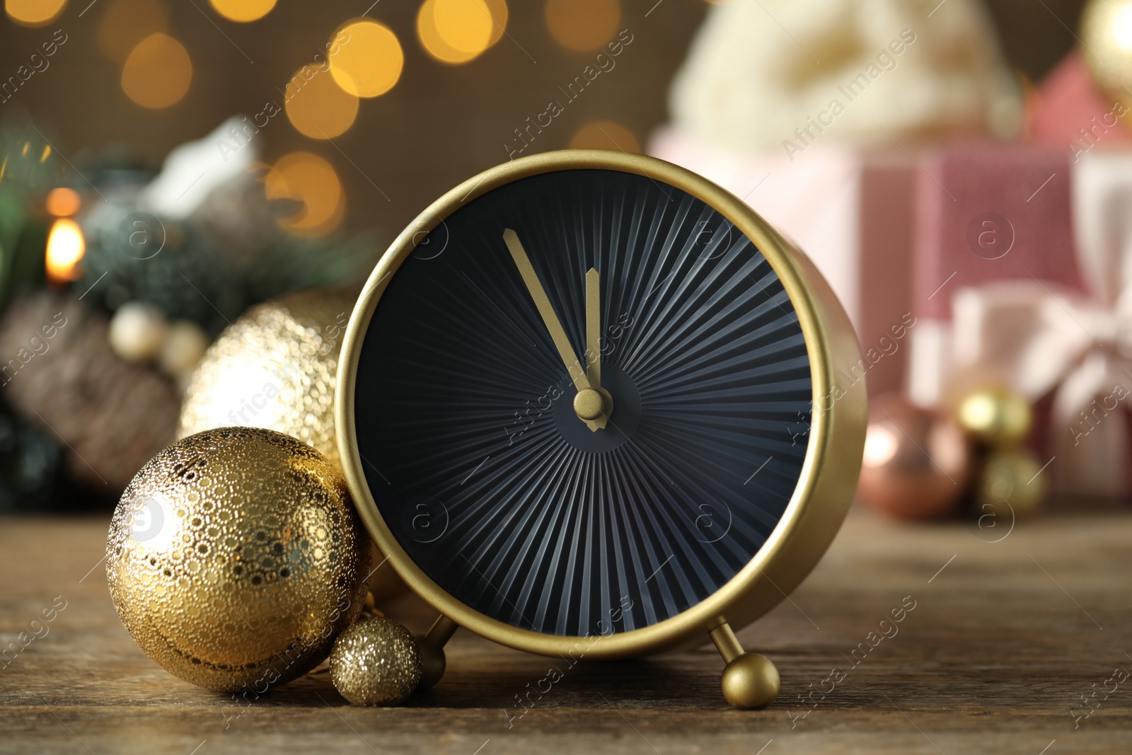 Photo of Stylish clock with decor on wooden table against blurred Christmas lights, closeup. New Year countdown