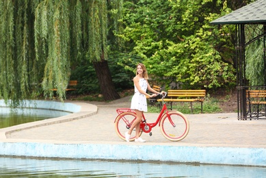 Beautiful woman in casual outfit with bicycle near pond outdoors