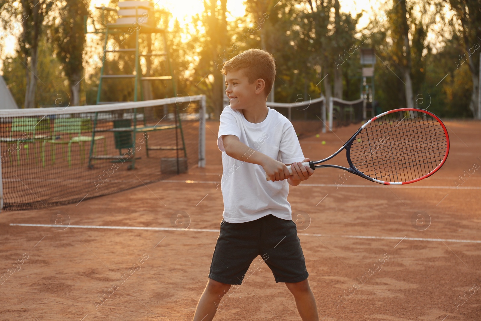 Photo of Cute little boy playing tennis on court outdoors