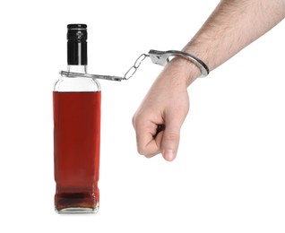 Photo of Addicted man in handcuffs with bottle of alcoholic drink on white background, closeup