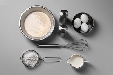 Photo of Flat lay composition with dough in bowl and metal whisk on grey background